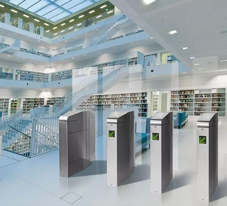 Bibliothèque moderne avec tourniquets et étagères remplies de livres, sous un éclairage naturel abondant.